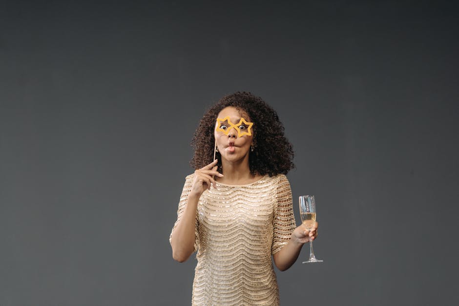 A cheerful woman in a sparkling dress poses with star-shaped glasses and a glass of champagne in a studio setting